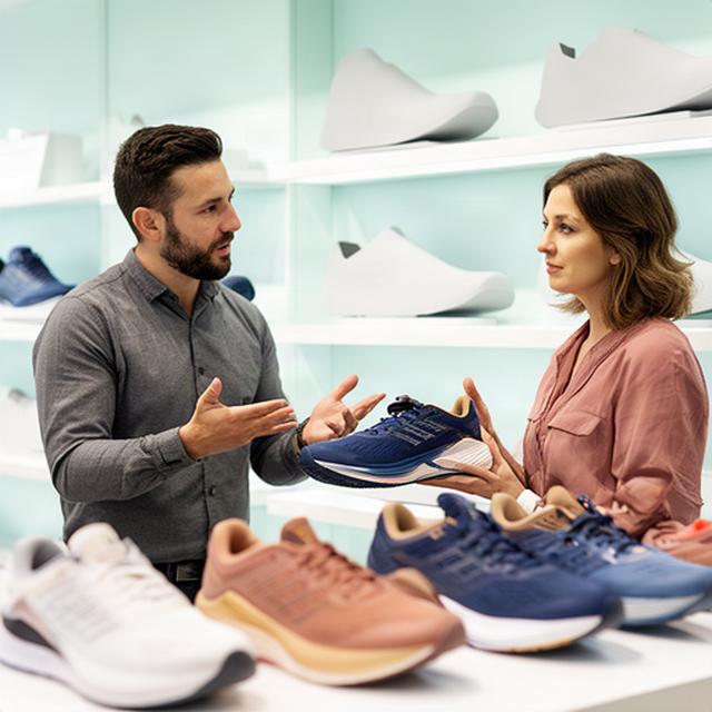 Sportadviseur bespreekt hardloopschoenen met klant bij een schoenenwand